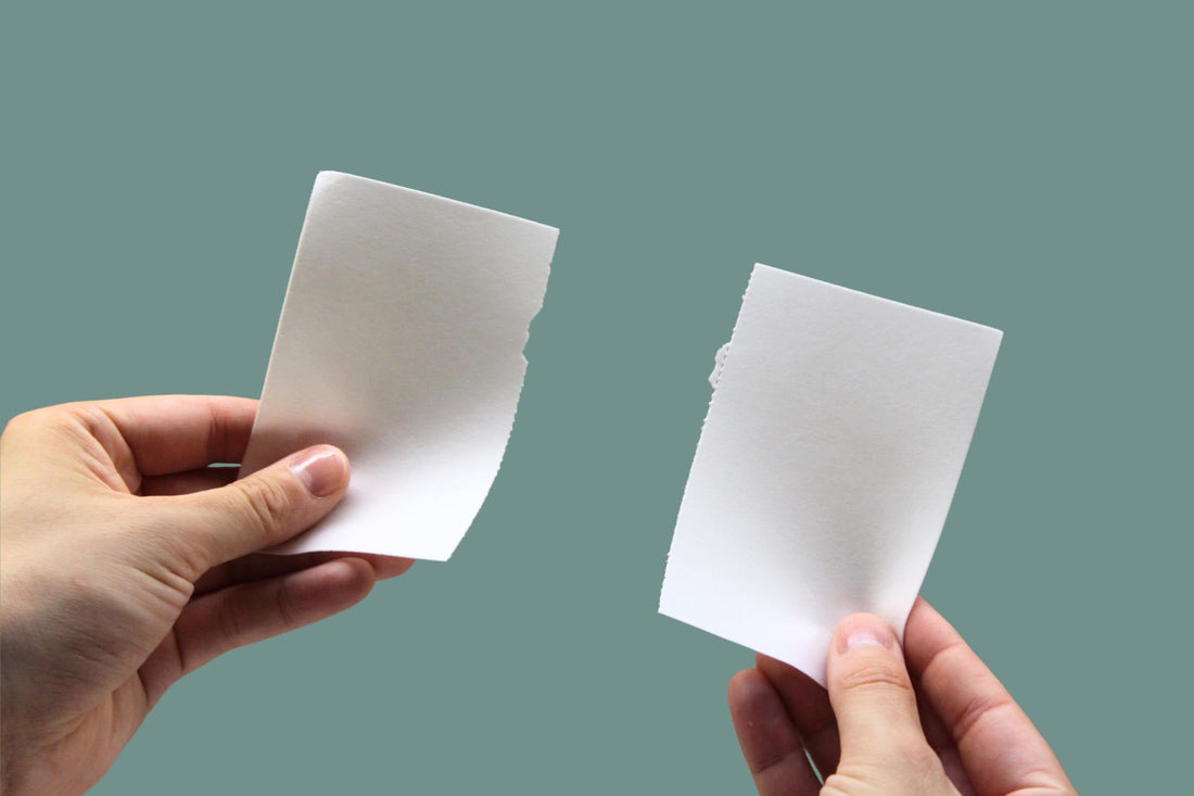 Two hands tearing a Blue Bird laundry detergent sheet in half